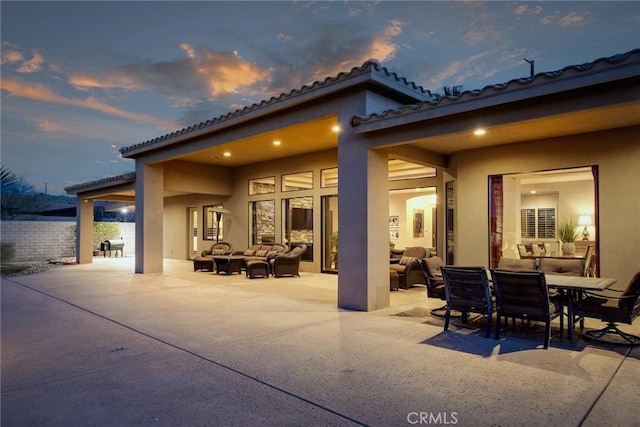 back house at dusk with an outdoor living space and a patio