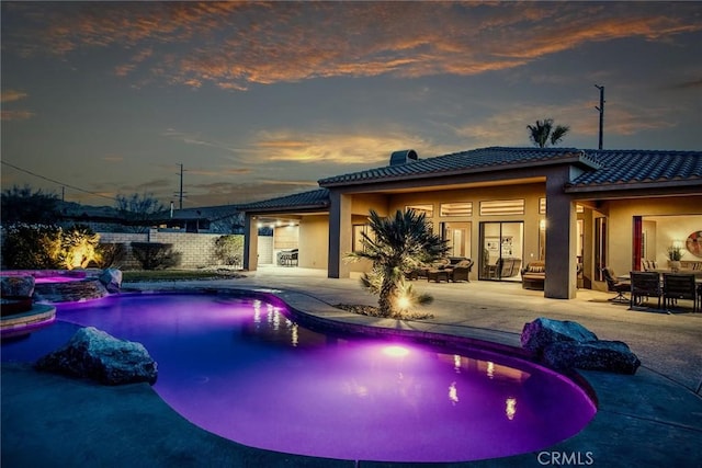 pool at dusk featuring an in ground hot tub, pool water feature, and a patio area