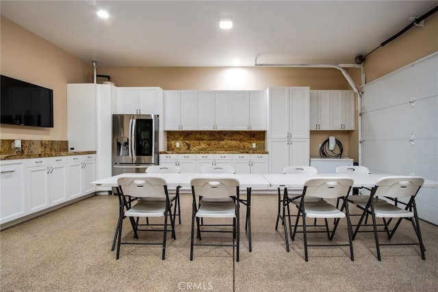 kitchen with stainless steel fridge with ice dispenser, backsplash, a breakfast bar, and white cabinets