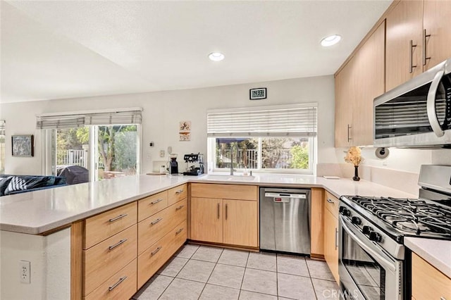 kitchen featuring sink, light tile patterned floors, appliances with stainless steel finishes, light brown cabinetry, and kitchen peninsula