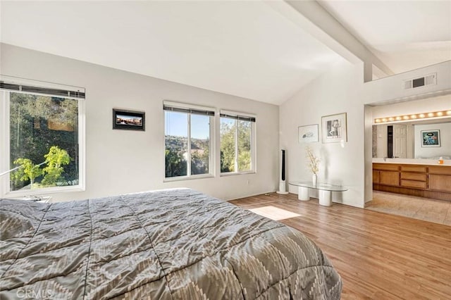 bedroom featuring ensuite bath, light hardwood / wood-style floors, and lofted ceiling with beams