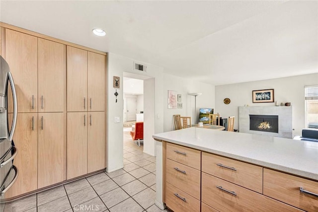 kitchen featuring light tile patterned flooring, stainless steel fridge, a fireplace, and light brown cabinetry