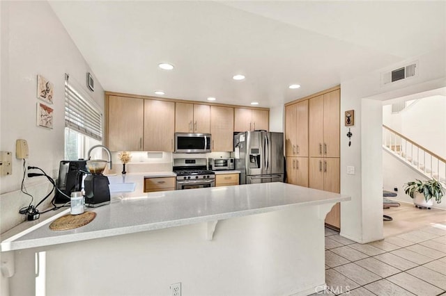 kitchen featuring a kitchen bar, stainless steel appliances, light tile patterned flooring, light brown cabinetry, and kitchen peninsula