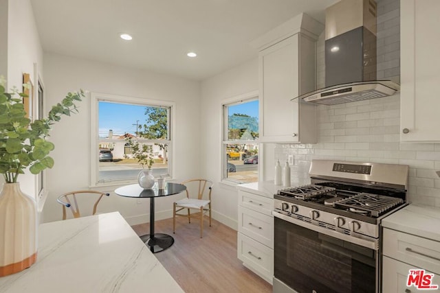 kitchen with stainless steel range with gas cooktop, white cabinets, light stone counters, and wall chimney exhaust hood