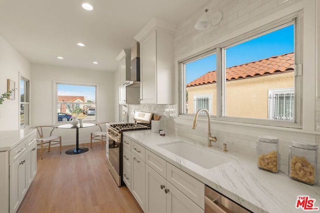 kitchen featuring stainless steel appliances, sink, wall chimney range hood, and white cabinets