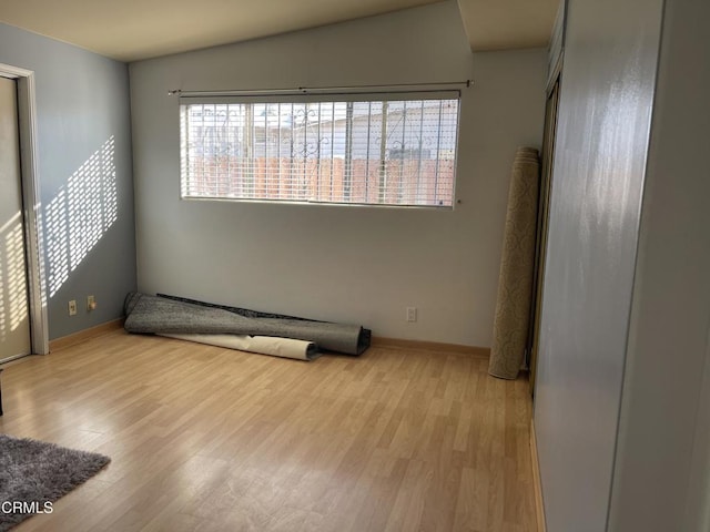 empty room featuring vaulted ceiling, light wood-style flooring, and baseboards