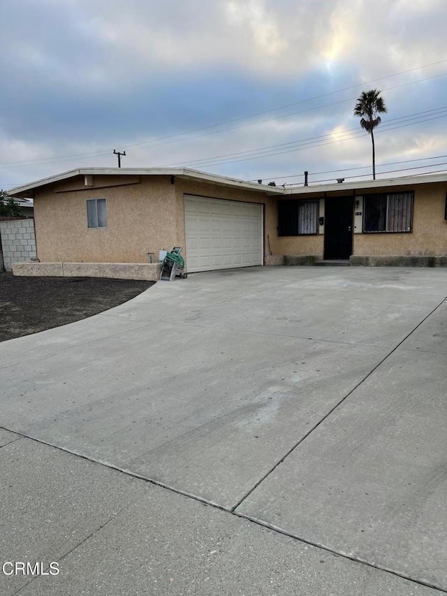 ranch-style house featuring a garage, concrete driveway, and stucco siding