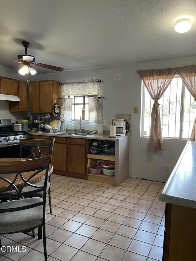 kitchen featuring brown cabinets, light tile patterned floors, gas stove, a sink, and under cabinet range hood