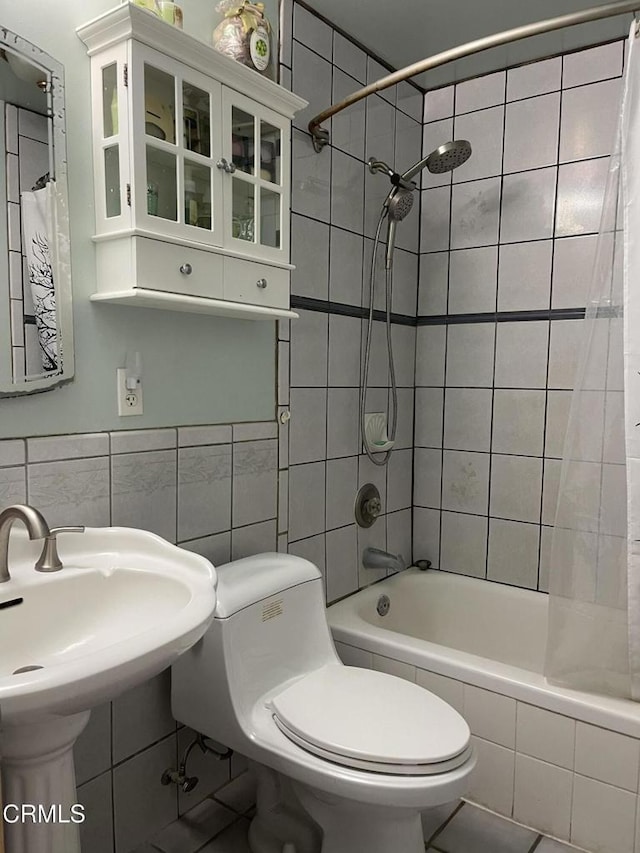 bathroom with toilet, a sink, tiled shower / bath, and tile walls