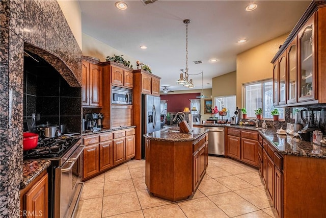 kitchen with light tile patterned floors, a kitchen island with sink, dark stone countertops, stainless steel appliances, and decorative light fixtures