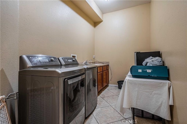 clothes washing area with light tile patterned floors, sink, washing machine and dryer, and cabinets