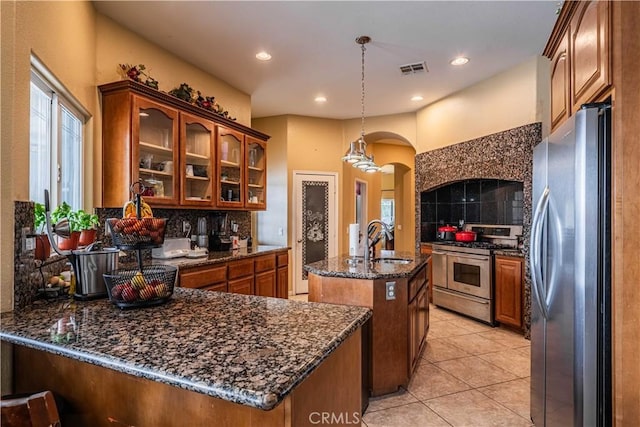 kitchen with appliances with stainless steel finishes, tasteful backsplash, an island with sink, sink, and hanging light fixtures