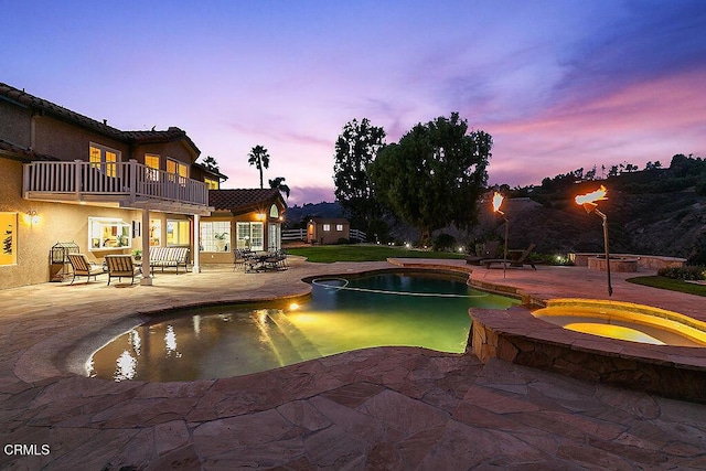 pool at dusk with a patio and an in ground hot tub