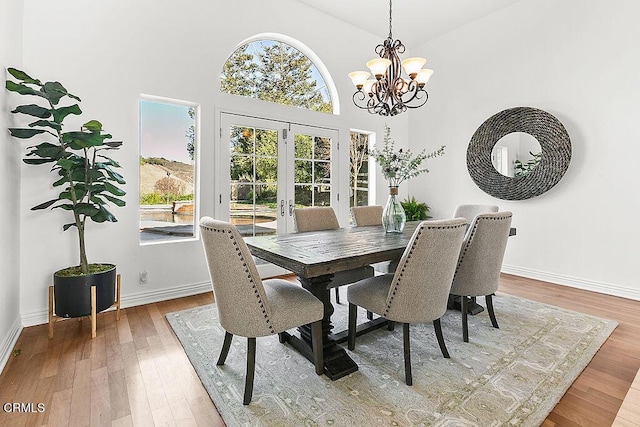 dining area with a high ceiling, wood-type flooring, an inviting chandelier, and french doors