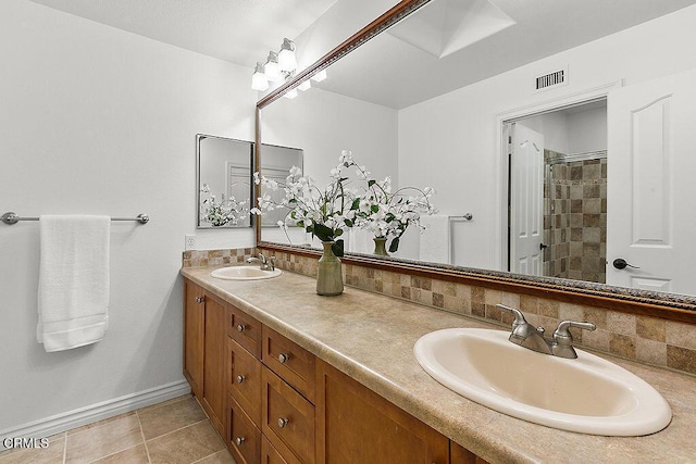 bathroom with tile patterned floors, a tile shower, vanity, and backsplash