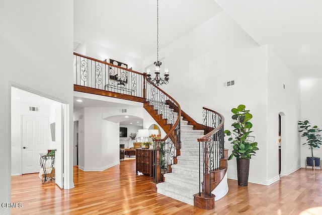 staircase with hardwood / wood-style floors, a towering ceiling, and a chandelier