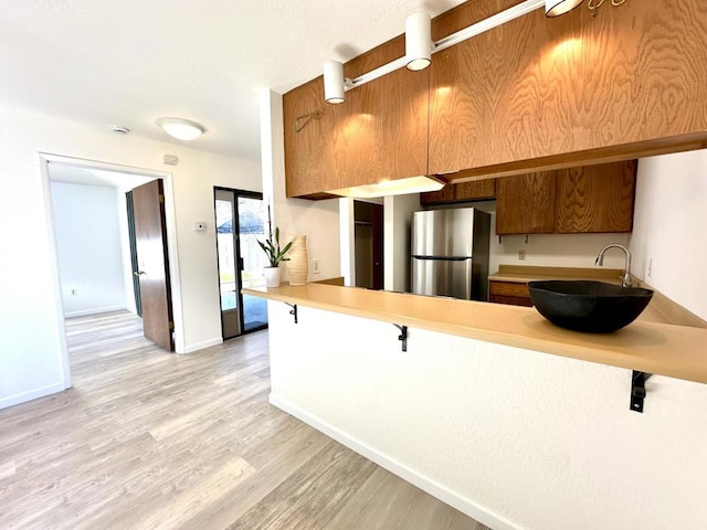 kitchen featuring sink, kitchen peninsula, stainless steel refrigerator, and light hardwood / wood-style flooring