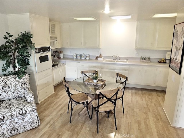 kitchen with white cabinetry, sink, white appliances, and light hardwood / wood-style floors