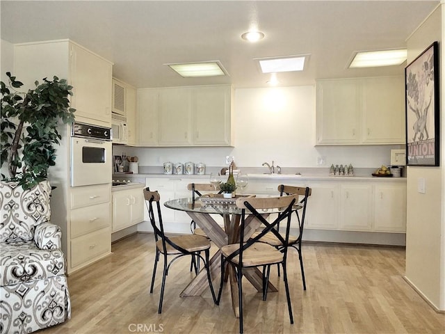 kitchen with white appliances, sink, light hardwood / wood-style flooring, and white cabinets