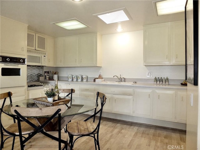 kitchen with sink, white appliances, white cabinets, and light wood-type flooring