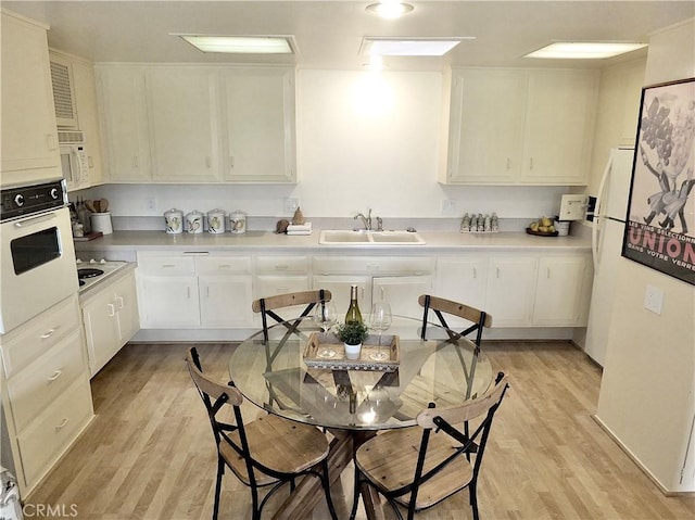 kitchen with sink, white cabinets, white appliances, and light hardwood / wood-style floors