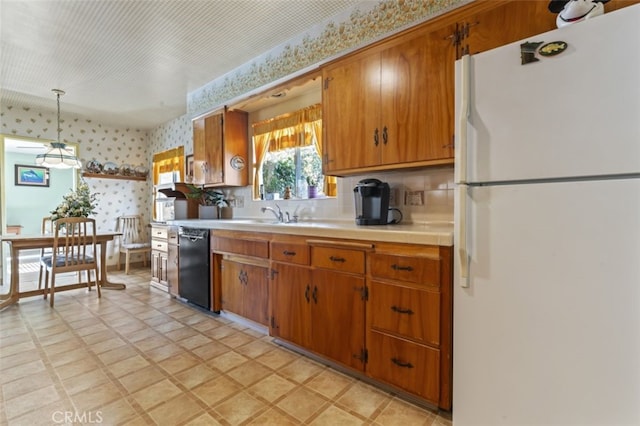 kitchen with black dishwasher, light countertops, freestanding refrigerator, wallpapered walls, and pendant lighting