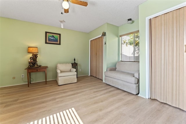 sitting room with light wood-type flooring, ceiling fan, and a textured ceiling