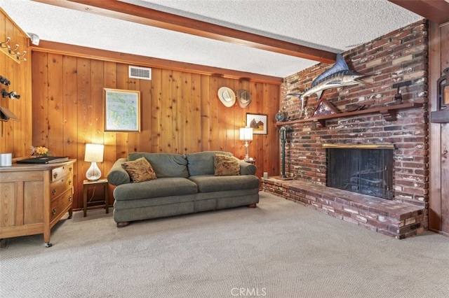 carpeted living area featuring beam ceiling, visible vents, a brick fireplace, wooden walls, and a textured ceiling