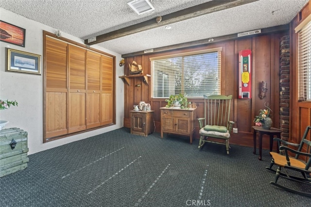 unfurnished room with a textured ceiling, beamed ceiling, dark carpet, and visible vents