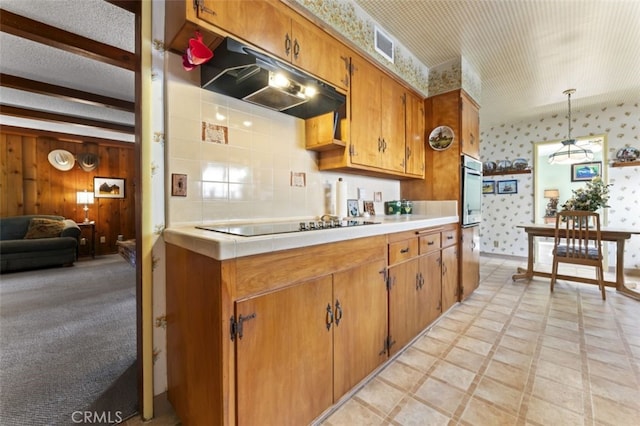 kitchen featuring wallpapered walls, brown cabinets, hanging light fixtures, light countertops, and under cabinet range hood