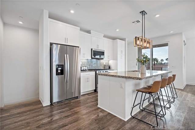 kitchen with appliances with stainless steel finishes, decorative light fixtures, tasteful backsplash, white cabinets, and a center island with sink