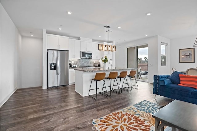 kitchen featuring a breakfast bar area, hanging light fixtures, stainless steel appliances, light stone counters, and a center island with sink