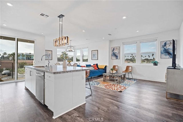 kitchen with pendant lighting, white cabinetry, an island with sink, sink, and light stone countertops