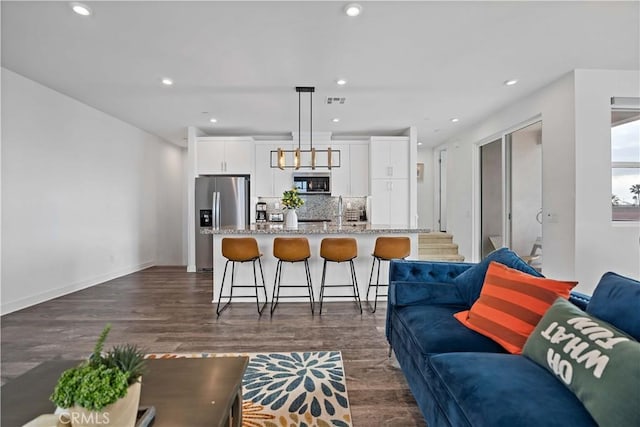 kitchen with appliances with stainless steel finishes, pendant lighting, white cabinetry, an island with sink, and a kitchen bar