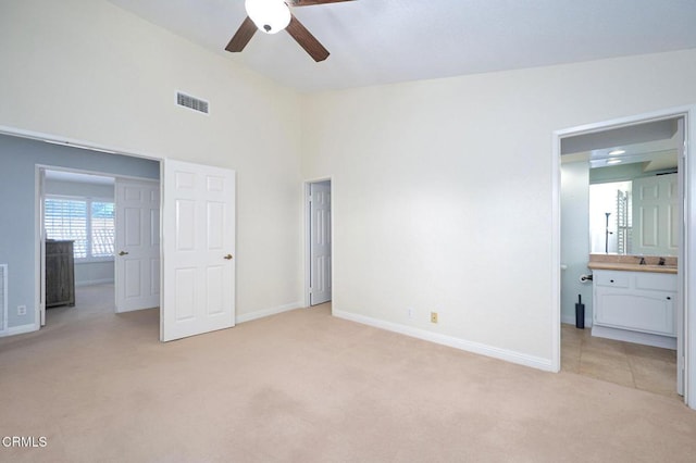 unfurnished bedroom featuring light carpet, connected bathroom, sink, and ceiling fan