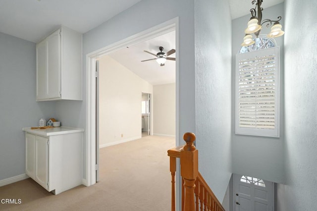 hallway with vaulted ceiling, light carpet, and an inviting chandelier