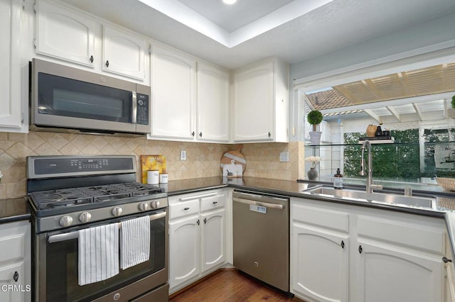 kitchen with appliances with stainless steel finishes, sink, white cabinets, backsplash, and dark wood-type flooring