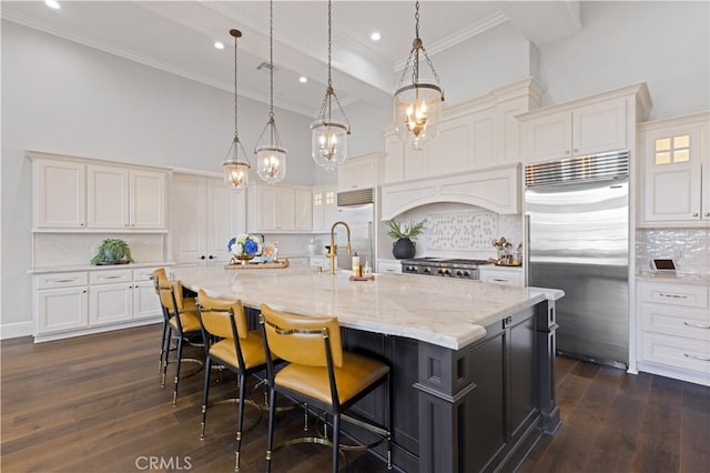 kitchen featuring a spacious island, tasteful backsplash, hanging light fixtures, built in fridge, and white cabinets