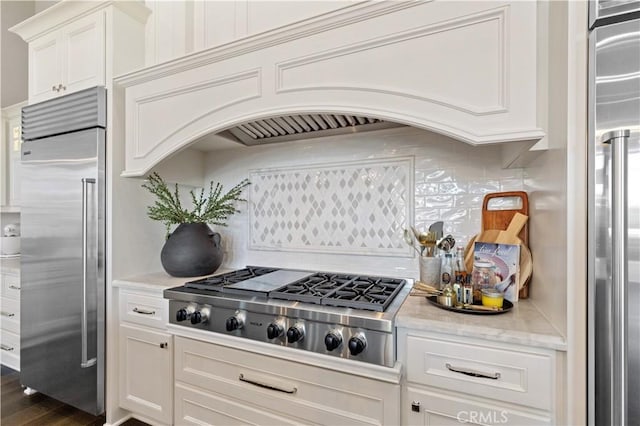 kitchen with white cabinetry, tasteful backsplash, range hood, and appliances with stainless steel finishes