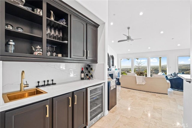 bar with sink, ceiling fan, backsplash, wine cooler, and light stone counters