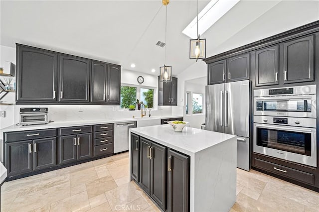 kitchen featuring lofted ceiling with skylight, a kitchen island, appliances with stainless steel finishes, decorative light fixtures, and tasteful backsplash