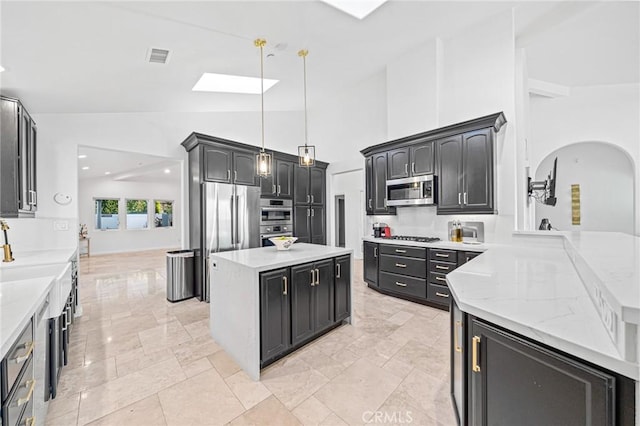 kitchen with light stone counters, decorative light fixtures, a skylight, kitchen peninsula, and stainless steel appliances