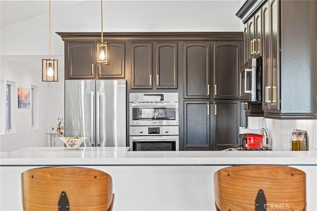 kitchen featuring vaulted ceiling, appliances with stainless steel finishes, dark brown cabinetry, and decorative light fixtures