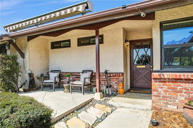 view of exterior entry with a patio, brick siding, and stucco siding