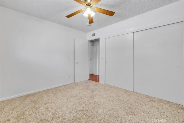 unfurnished bedroom featuring visible vents, carpet, a closet, a textured ceiling, and a ceiling fan