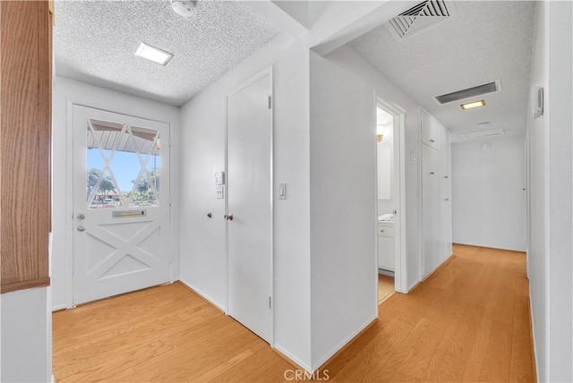 hallway featuring light wood finished floors, visible vents, and a textured ceiling