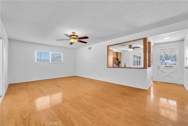 spare room featuring visible vents, light wood-style floors, a healthy amount of sunlight, and a textured ceiling