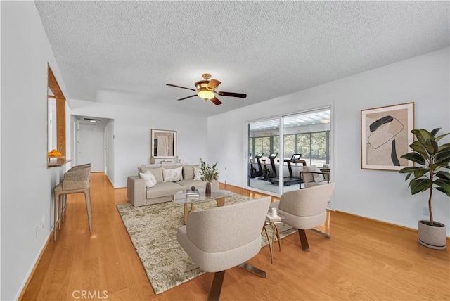 living room with a ceiling fan, light wood-style floors, baseboards, and a textured ceiling