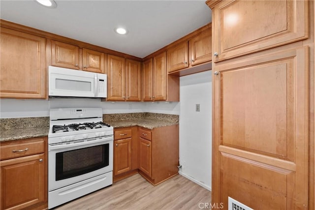 kitchen with stone countertops, white appliances, and light wood-type flooring