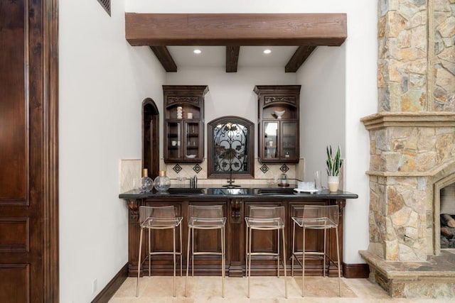 bar featuring beamed ceiling, backsplash, and dark brown cabinetry